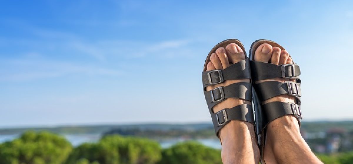 Male feet in leather slippers relaxing on balcony of summer vacation resort hotel in sunny morning