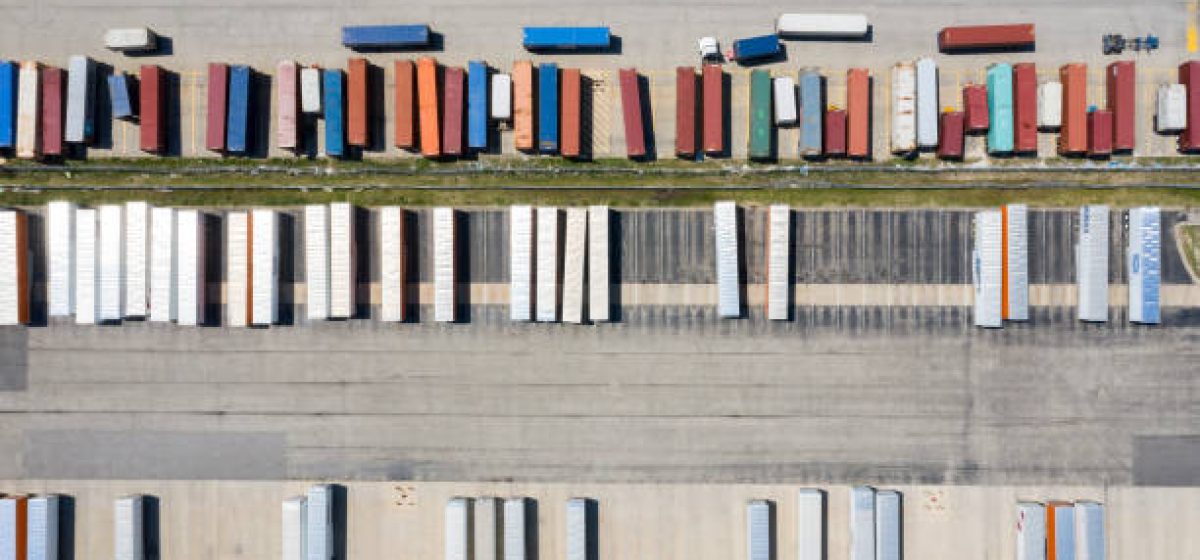 Aerial view of a large group of containers and trucks during unloading in front of a large, modern warehouse in Illinois, United States.