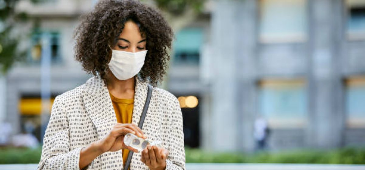 Businesswoman cleaning hand with sanitizer in city. Entrepreneur wearing mask standing outdoors during pandemic. She is in formals.