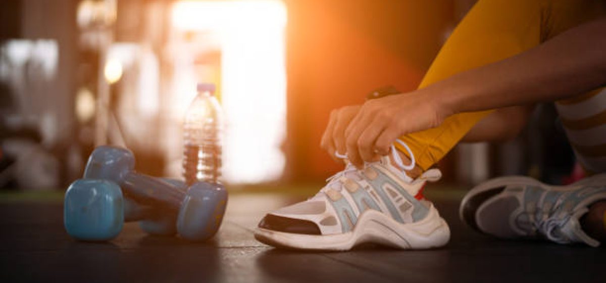 Young sporty woman with smart watch tying shoelaces in fitness