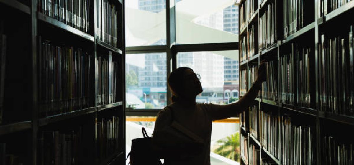 female student in silhouette looking at the books from the bookshelf