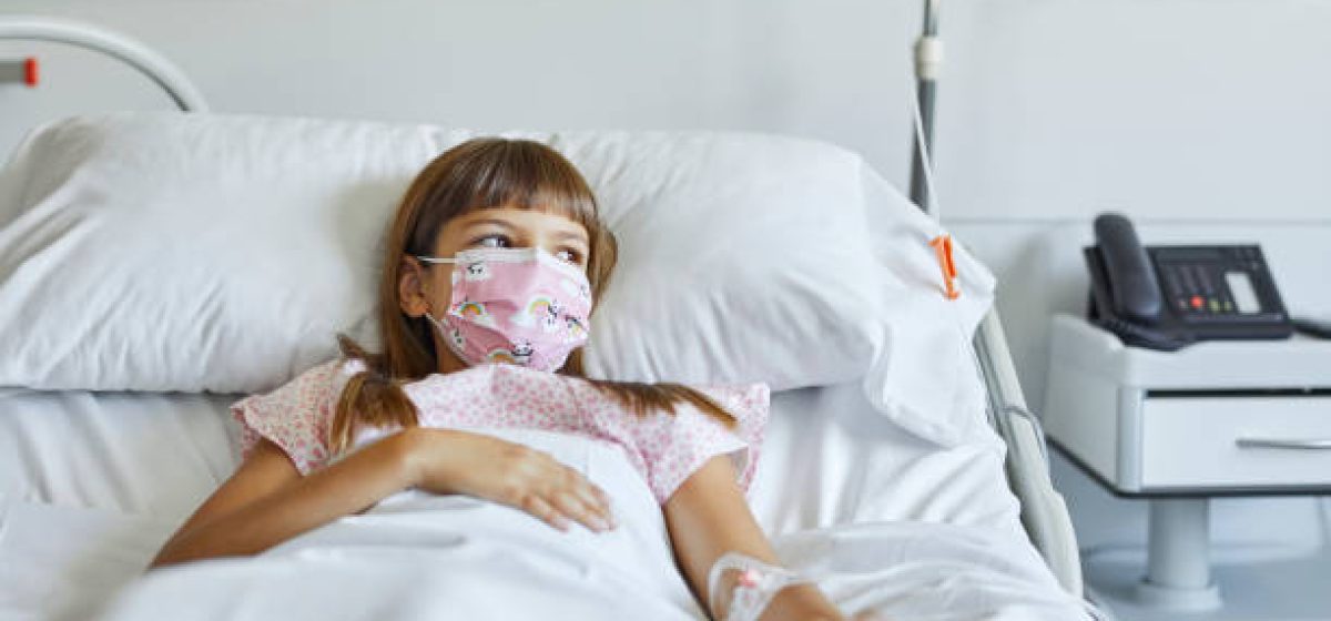 Sick girl lying on bed in ICU. Female patient is looking away while wearing protective face mask. She is in hospital during COVID-19 pandemic.
