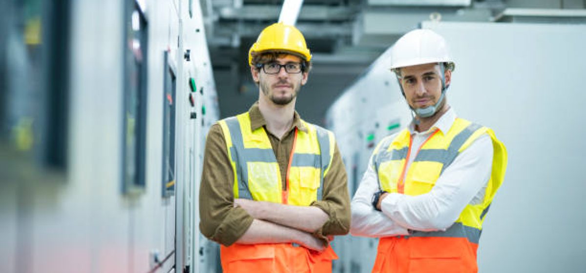 Energy management system (EMS) concept. Portrait of  Industrial service electrician engineers standing side by side while working in electricity control room for power plant.