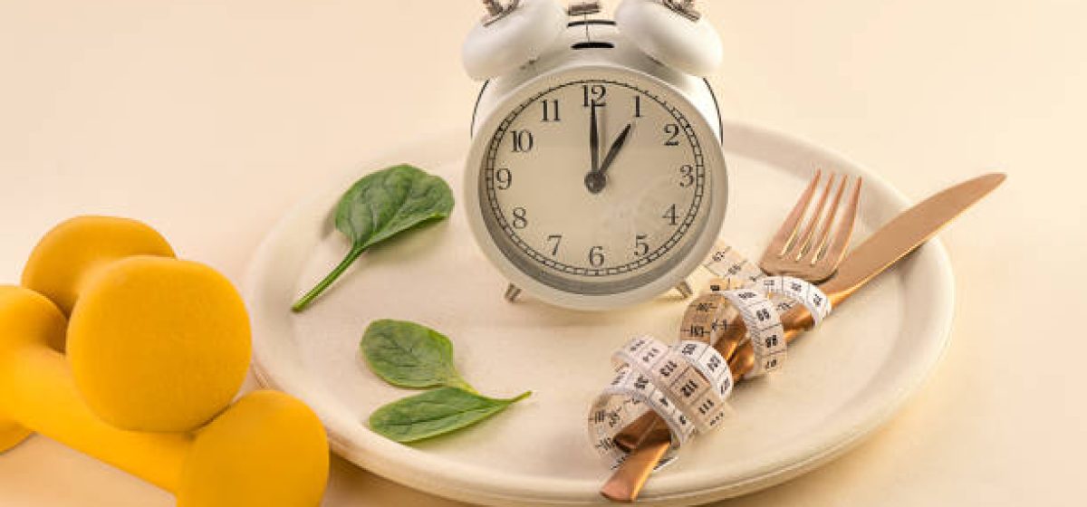 Healthy food Composition with cutlery, plate, measuring tape, yellow dumbbell, green vegetable salad leaves and alarm clock on pastel beige background. Dieting and keep fit. Close-up. Copy space. Front view.