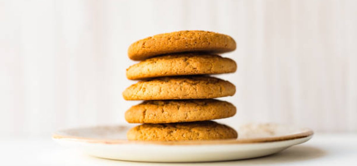 Oatmeal cookies stack on red plate on white wooden table against light wall background. Close up. Selective soft focus. Shallow depth of field. Text copy space.