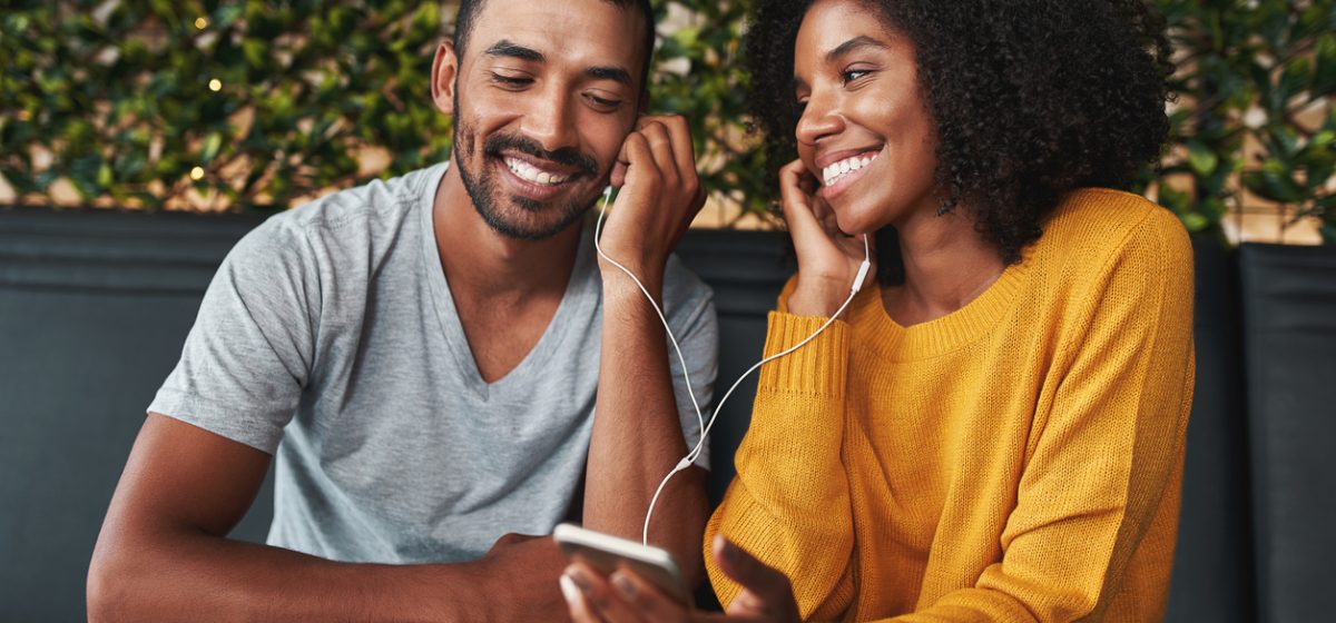 Portrait of an african young couple together listening music in cafe on one earphone